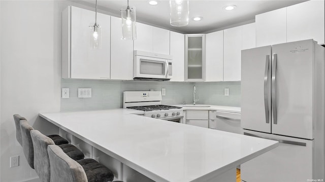 kitchen with kitchen peninsula, decorative light fixtures, white appliances, white cabinets, and a kitchen bar