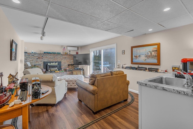 living area with a drop ceiling, a wall unit AC, recessed lighting, rail lighting, and dark wood-style flooring