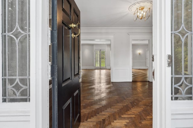 foyer entrance with crown molding, dark parquet floors, and an inviting chandelier