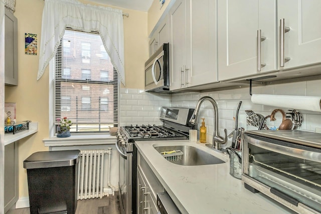 kitchen with a toaster, decorative backsplash, radiator, stainless steel appliances, and a sink