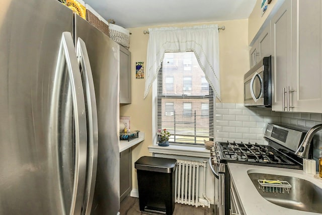 kitchen featuring light countertops, appliances with stainless steel finishes, tasteful backsplash, radiator heating unit, and dark wood finished floors