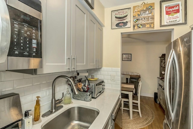 kitchen featuring dark wood-type flooring, a sink, light countertops, appliances with stainless steel finishes, and backsplash