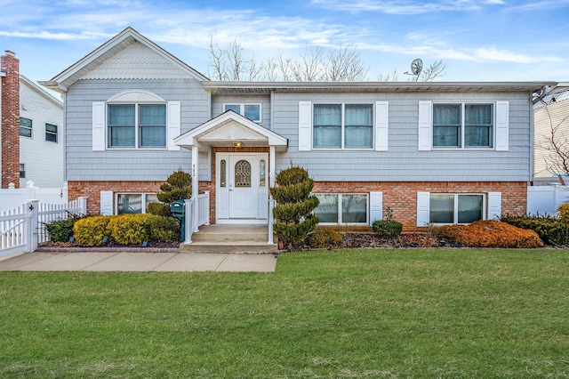 raised ranch with a front yard, fence, and brick siding