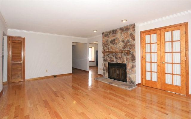 unfurnished living room with light wood-style flooring, crown molding, a stone fireplace, and french doors