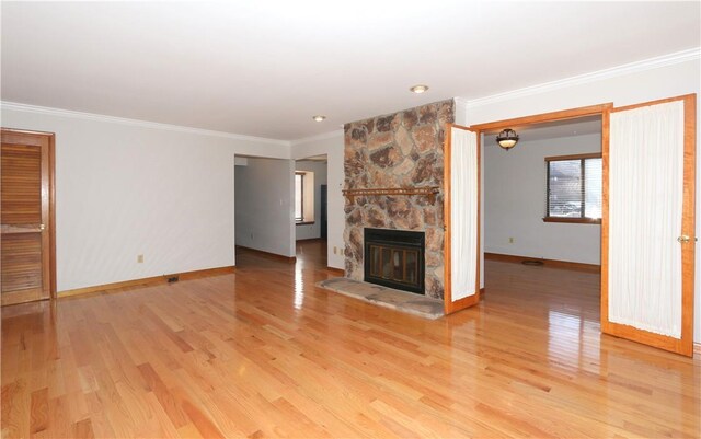 unfurnished living room with light wood-style floors, baseboards, ornamental molding, and a stone fireplace