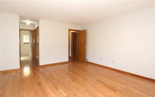 unfurnished room with light wood finished floors, visible vents, and baseboards