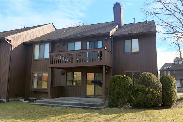 rear view of property featuring roof with shingles, a yard, a chimney, a patio area, and a balcony