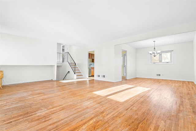 unfurnished living room featuring visible vents, an inviting chandelier, light wood-style floors, baseboards, and stairs