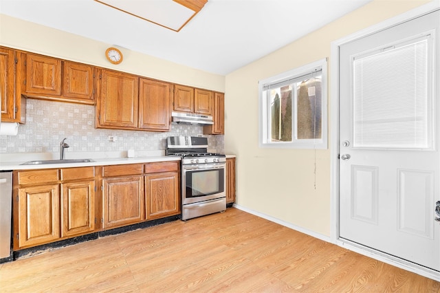 kitchen with stainless steel appliances, light countertops, brown cabinetry, a sink, and under cabinet range hood