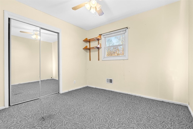 unfurnished bedroom featuring baseboards, visible vents, a ceiling fan, dark carpet, and a closet