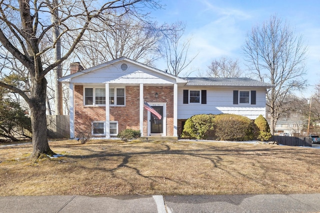 bi-level home with brick siding, a chimney, a front lawn, and fence