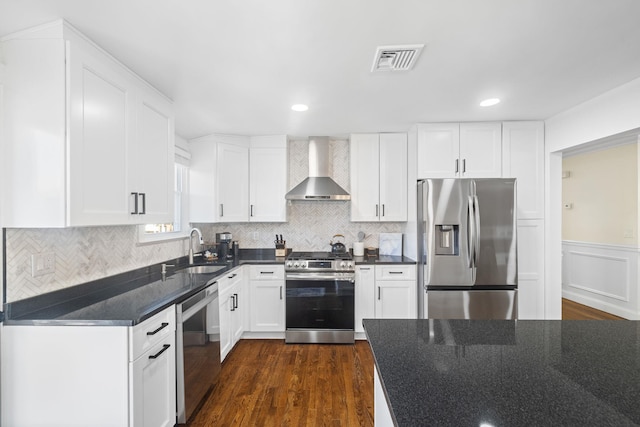 kitchen with visible vents, white cabinets, wall chimney exhaust hood, appliances with stainless steel finishes, and a sink