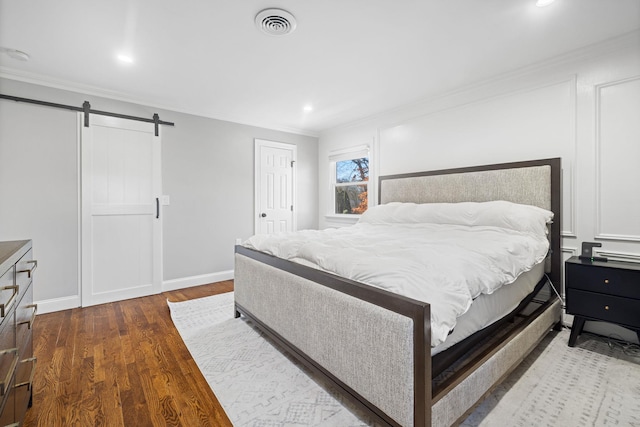 bedroom featuring ornamental molding, wood finished floors, visible vents, and a barn door