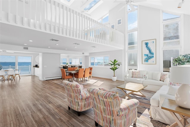 living room featuring light hardwood / wood-style flooring, a water view, a towering ceiling, ceiling fan, and baseboard heating