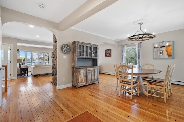 dining area featuring arched walkways, light wood-style flooring, a baseboard radiator, baseboards, and a notable chandelier
