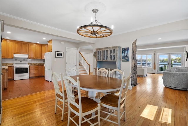 dining space with arched walkways, recessed lighting, light wood finished floors, a notable chandelier, and stairs
