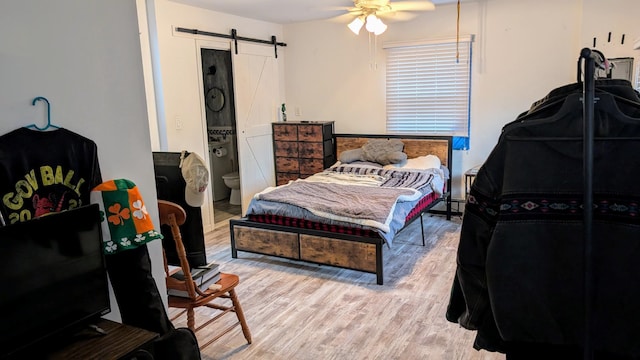 bedroom featuring ensuite bathroom, a ceiling fan, a baseboard heating unit, wood finished floors, and a barn door