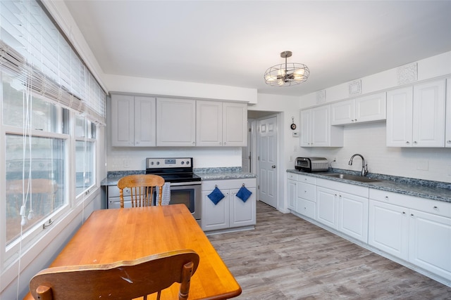 kitchen with stainless steel range with electric cooktop, a sink, a chandelier, tasteful backsplash, and light wood finished floors