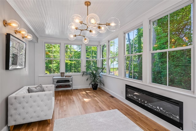 sunroom with a wealth of natural light, a glass covered fireplace, visible vents, and an inviting chandelier