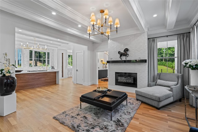 living area with beam ceiling, crown molding, a notable chandelier, light wood finished floors, and a tiled fireplace