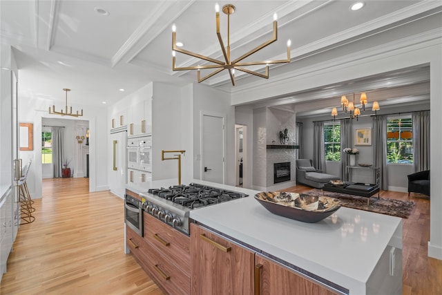 kitchen with a notable chandelier, stainless steel gas cooktop, a large fireplace, light wood finished floors, and crown molding