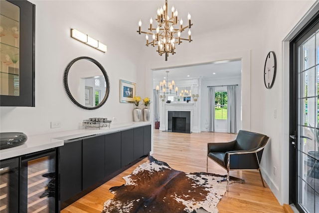 bar featuring beverage cooler, a fireplace with flush hearth, decorative light fixtures, an inviting chandelier, and light wood-type flooring