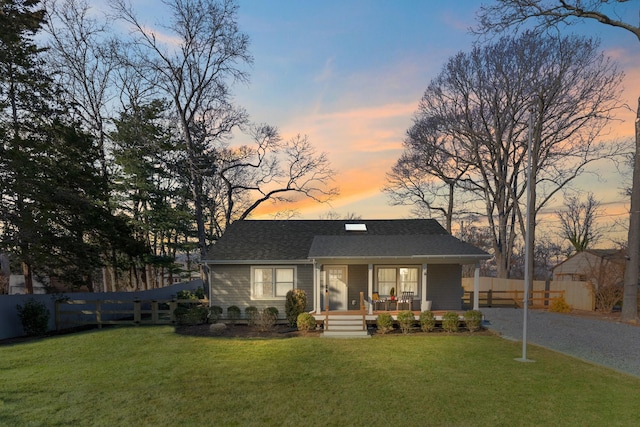 back house at dusk featuring a lawn and a porch