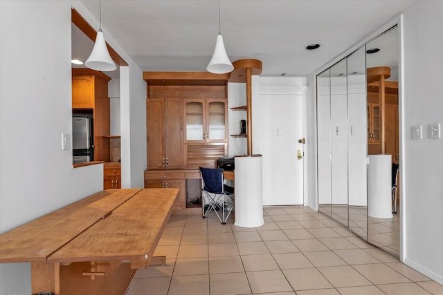 kitchen featuring light tile patterned floors, hanging light fixtures, open shelves, stainless steel refrigerator, and glass insert cabinets