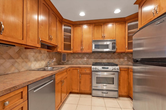 kitchen with a sink, light tile patterned floors, light countertops, appliances with stainless steel finishes, and glass insert cabinets