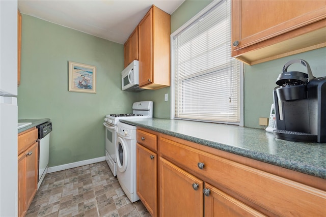 kitchen with brown cabinetry, stone finish flooring, washer / dryer, white appliances, and baseboards