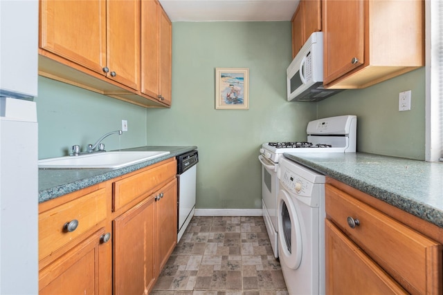 kitchen with washing machine and clothes dryer, brown cabinetry, a sink, white appliances, and baseboards