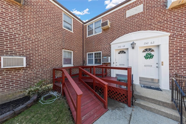 property entrance featuring a wall unit AC, a wooden deck, and brick siding