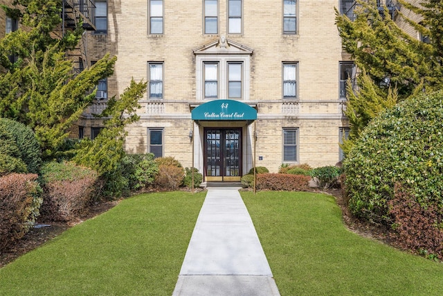 doorway to property featuring a lawn, french doors, and brick siding