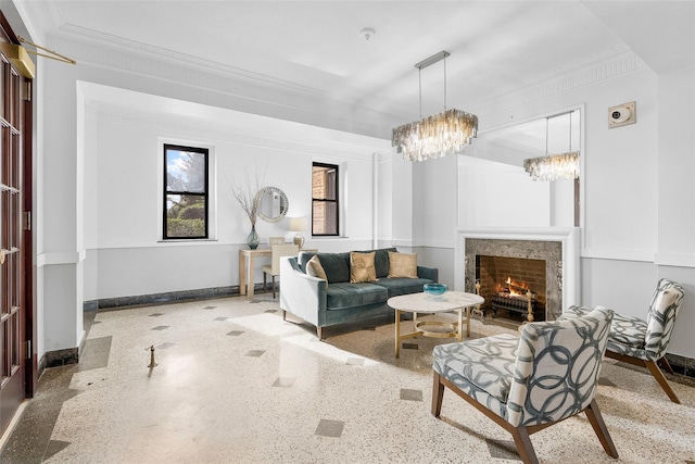 living area featuring baseboards, crown molding, speckled floor, a chandelier, and a high end fireplace