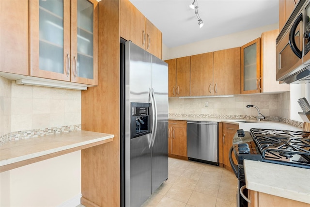 kitchen featuring glass insert cabinets, light countertops, stainless steel appliances, and a sink