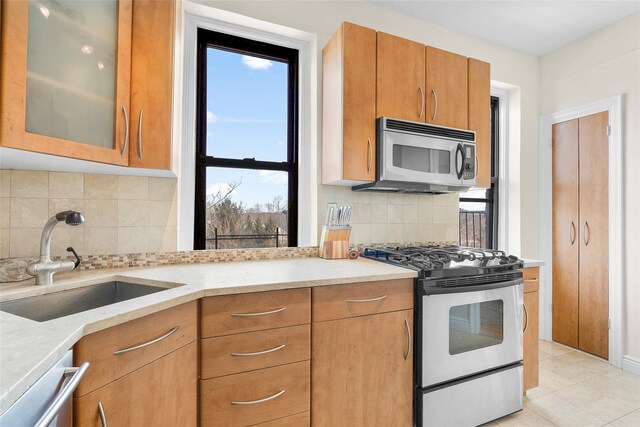 kitchen with glass insert cabinets, appliances with stainless steel finishes, decorative backsplash, and a sink