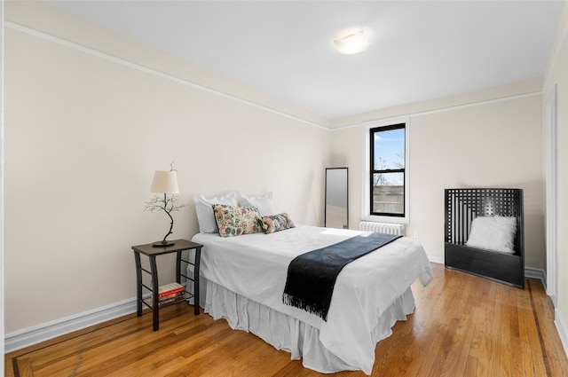 bedroom with radiator heating unit, light wood-type flooring, and baseboards