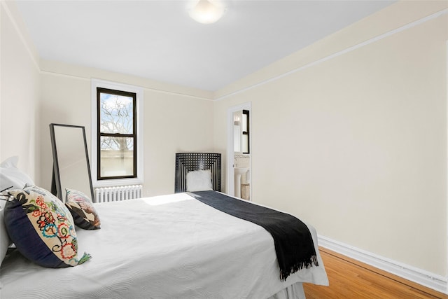 bedroom with radiator, ensuite bathroom, baseboards, and wood finished floors