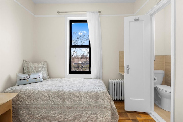 bedroom with wood finished floors, tile walls, and radiator