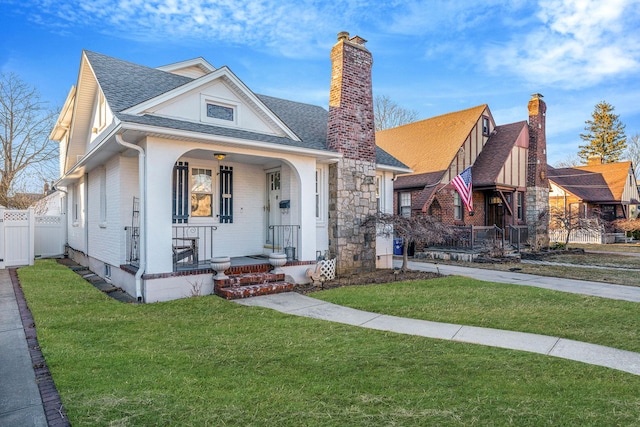 view of front of house with a chimney, roof with shingles, covered porch, fence, and a front yard