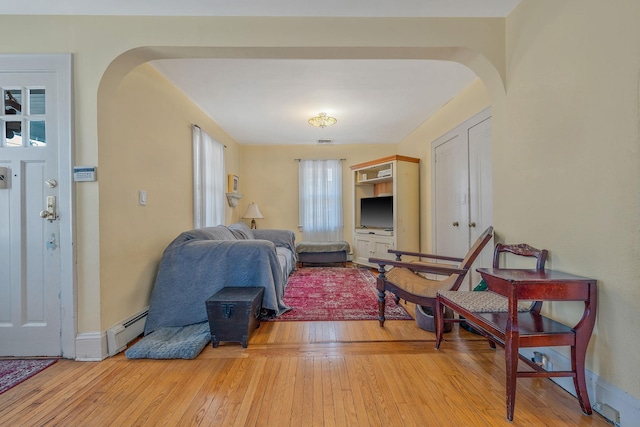 living area featuring arched walkways, visible vents, baseboard heating, light wood-type flooring, and baseboards