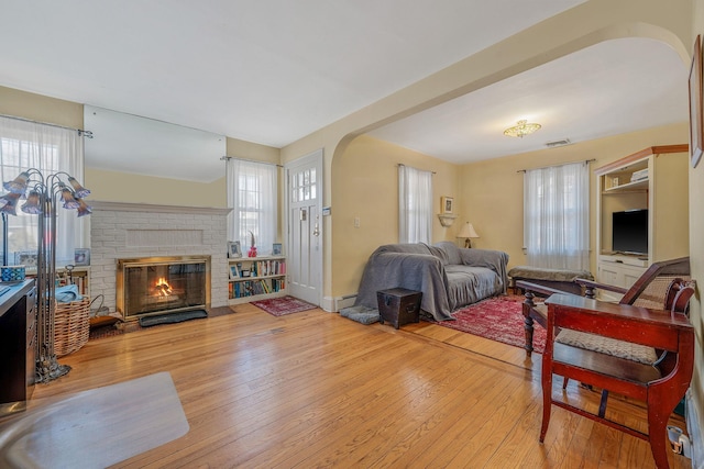 living area with arched walkways, a baseboard radiator, visible vents, a brick fireplace, and hardwood / wood-style floors