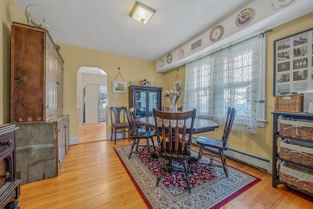 dining space with light wood-type flooring, visible vents, and arched walkways