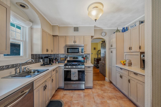 kitchen with stainless steel appliances, arched walkways, a sink, and wallpapered walls