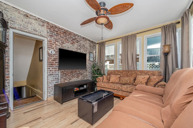 living area with brick wall, light wood-style flooring, and a ceiling fan