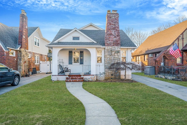 bungalow-style home featuring roof with shingles, a chimney, covered porch, fence, and a front lawn