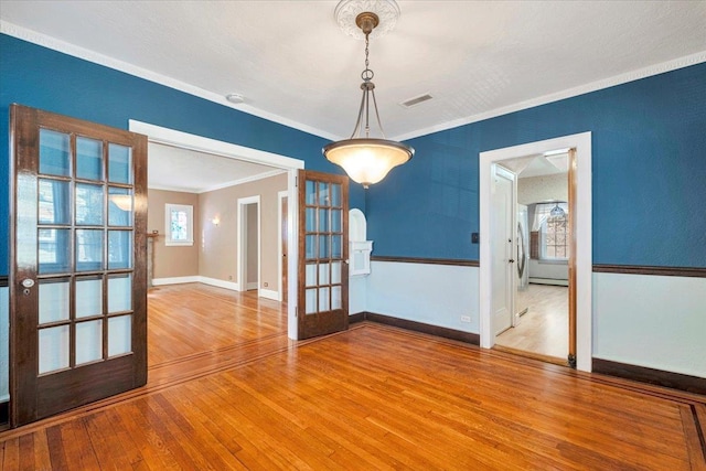 unfurnished dining area with baseboards, visible vents, ornamental molding, wood finished floors, and french doors