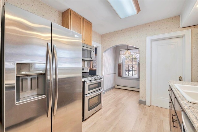 kitchen with arched walkways, a baseboard radiator, light wood-style floors, light countertops, and appliances with stainless steel finishes