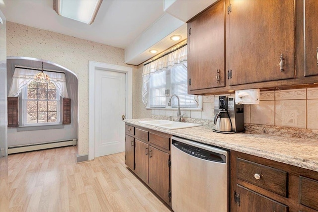 kitchen with decorative backsplash, dishwasher, baseboard heating, light wood-style floors, and a sink