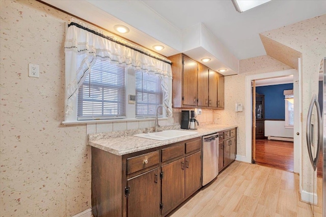 kitchen with stainless steel appliances, light countertops, a sink, light wood-type flooring, and wallpapered walls